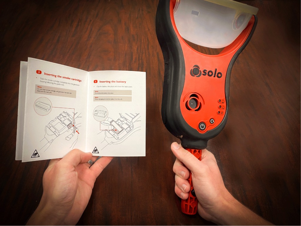 hand holding a solo 365 electronic smoke detector tester and a user manual
